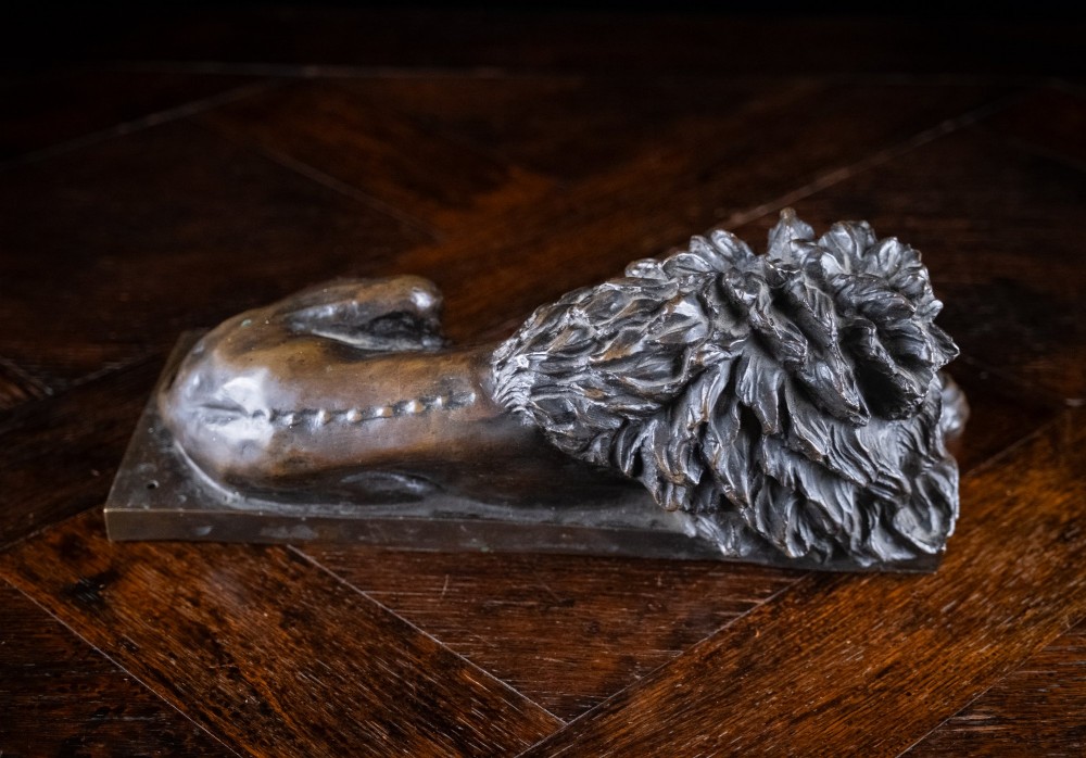 A dark brown patinated bronze sculpture depicting a recumbent sleeping lion resting its head on an integrated rectangular base. View V