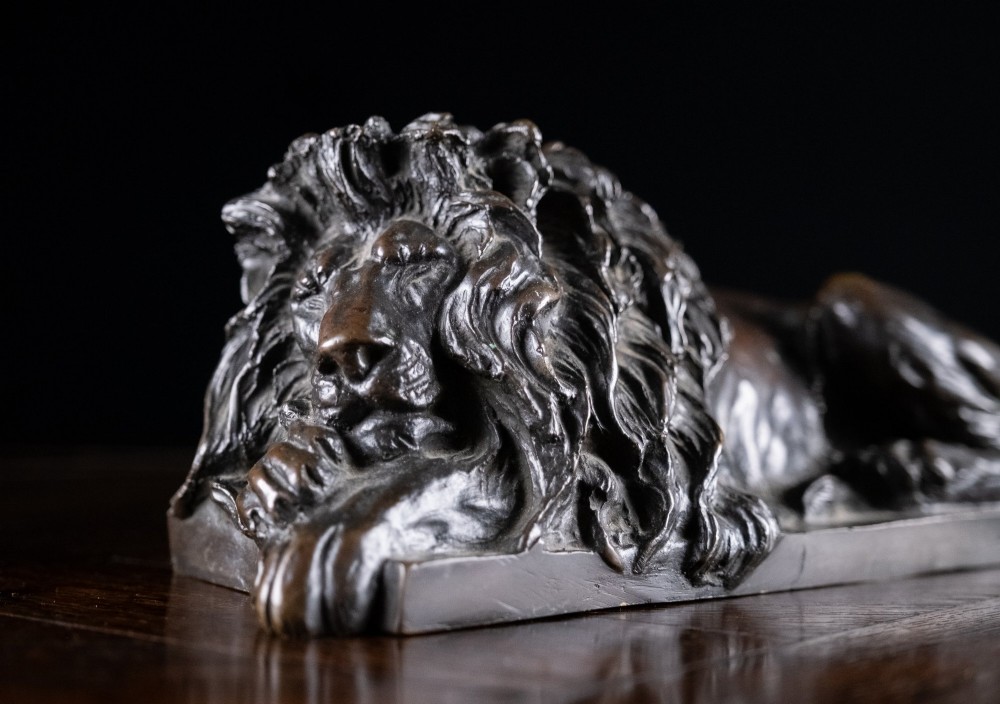 A dark brown patinated bronze sculpture depicting a recumbent sleeping lion resting its head on an integrated rectangular base. View VIII