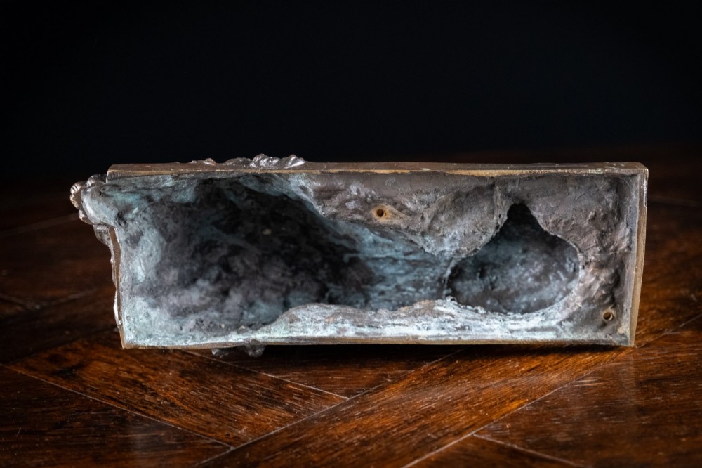 A dark brown patinated bronze sculpture depicting a recumbent sleeping lion resting its head on an integrated rectangular base. View XII