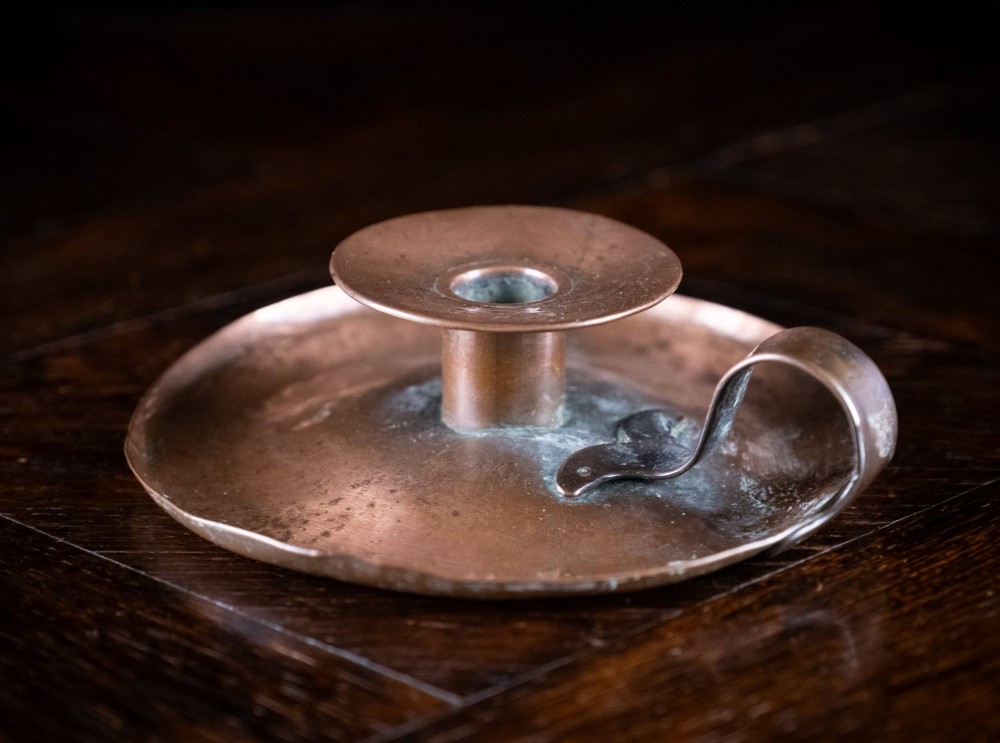 A copper Arts and Crafts chamberstick with a wide dish base, cylindrical candle sconce, and a looped metal handle. View II