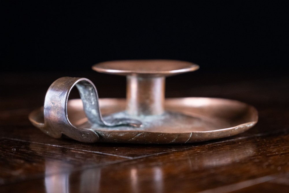 A copper Arts and Crafts chamberstick with a wide dish base, cylindrical candle sconce, and a looped metal handle. View III