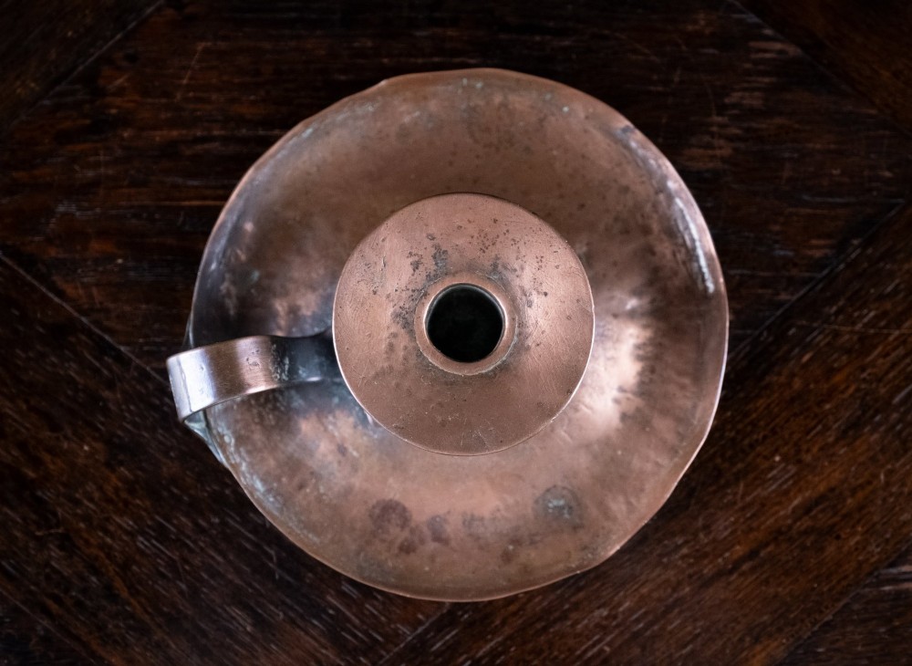 A copper Arts and Crafts chamberstick with a wide dish base, cylindrical candle sconce, and a looped metal handle. View IV