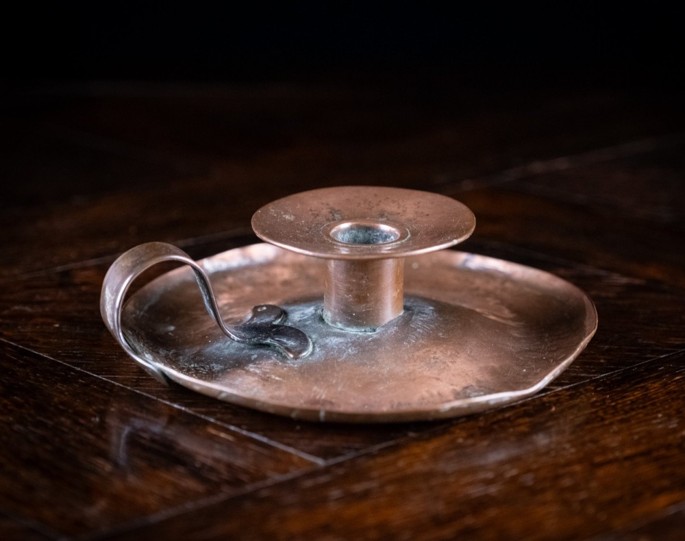 A copper Arts and Crafts chamberstick with a wide dish base, cylindrical candle sconce, and a looped metal handle. View V