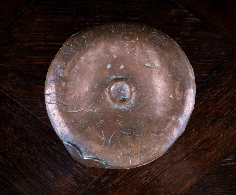 A copper Arts and Crafts chamberstick with a wide dish base, cylindrical candle sconce, and a looped metal handle. View VI