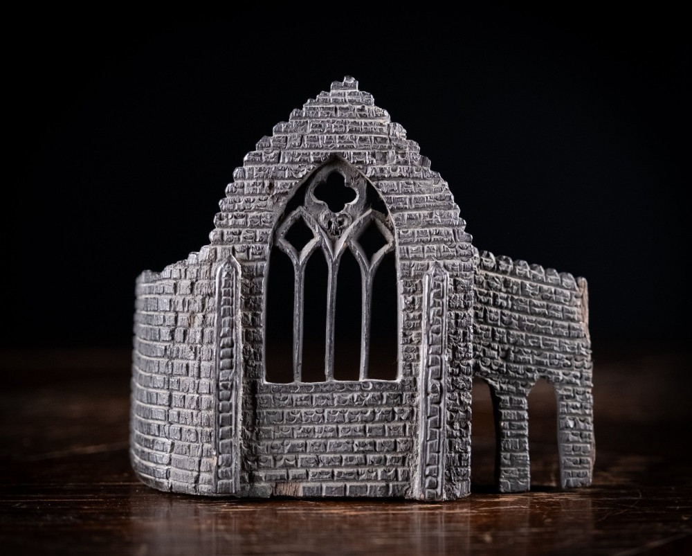 A dark hand-carved bog oak miniature representing a Gothic abbey architectural ruin with a tracery window and relief masonry wall.