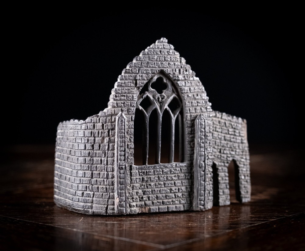 A dark hand-carved bog oak miniature representing a Gothic abbey architectural ruin with a tracery window and relief masonry wall. View III