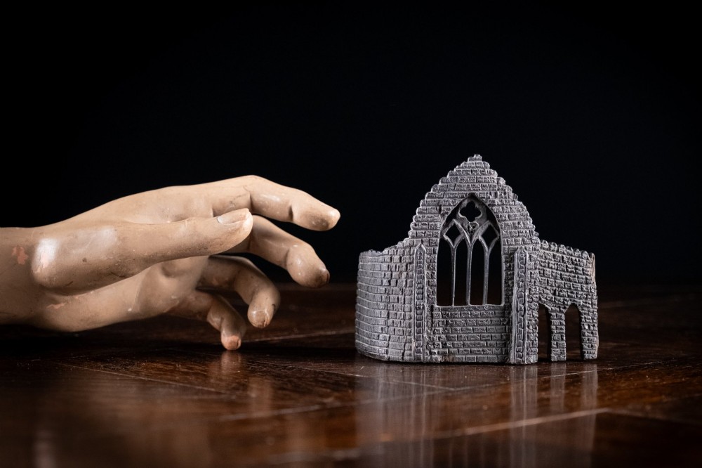 A dark hand-carved bog oak miniature representing a Gothic abbey architectural ruin with a tracery window and relief masonry wall. View V