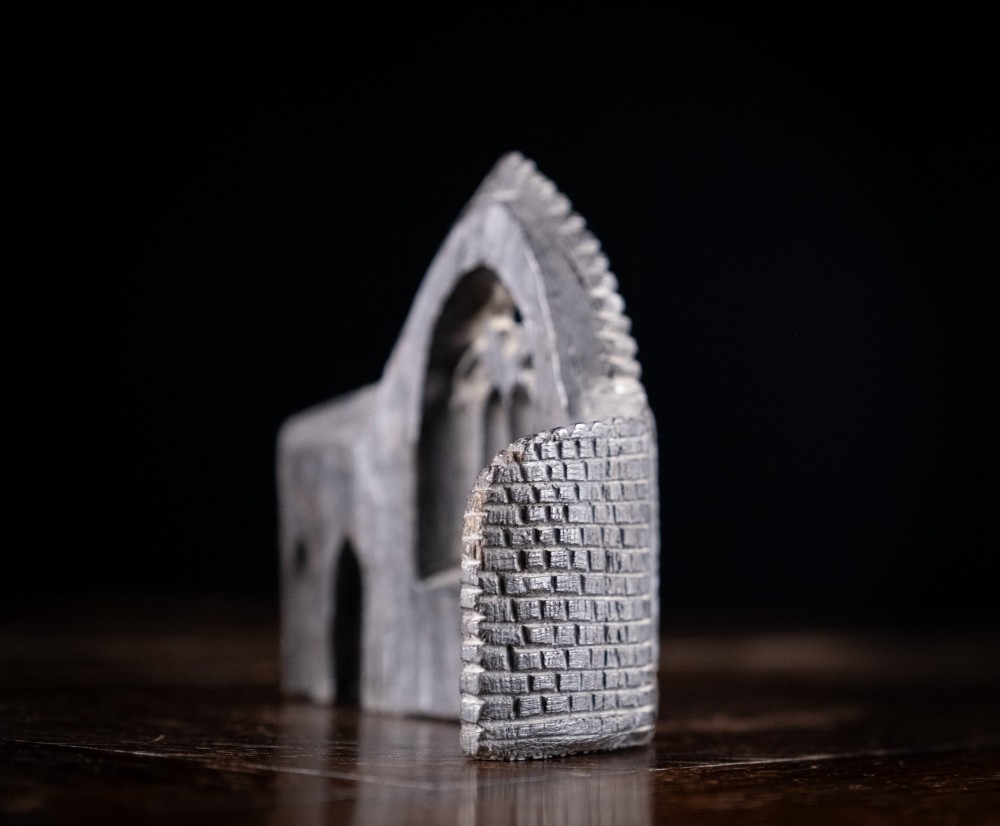 A dark hand-carved bog oak miniature representing a Gothic abbey architectural ruin with a tracery window and relief masonry wall. View VI