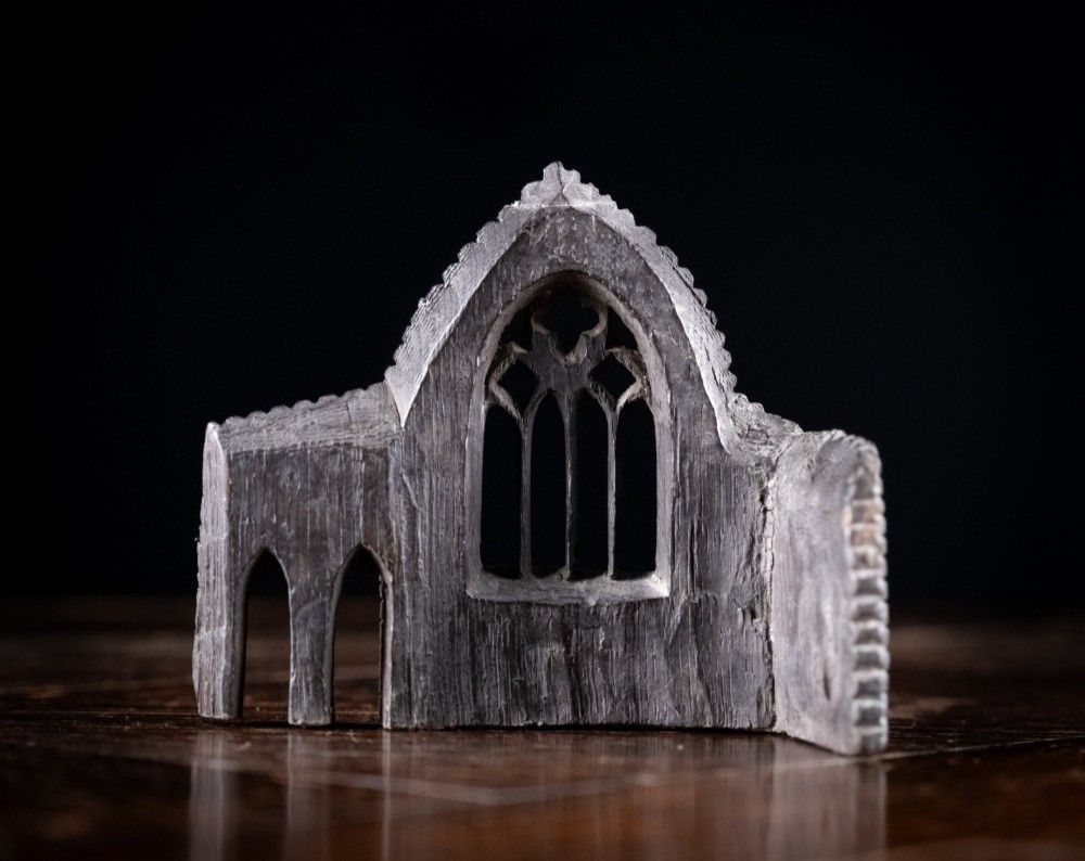 A dark hand-carved bog oak miniature representing a Gothic abbey architectural ruin with a tracery window and relief masonry wall. View VII
