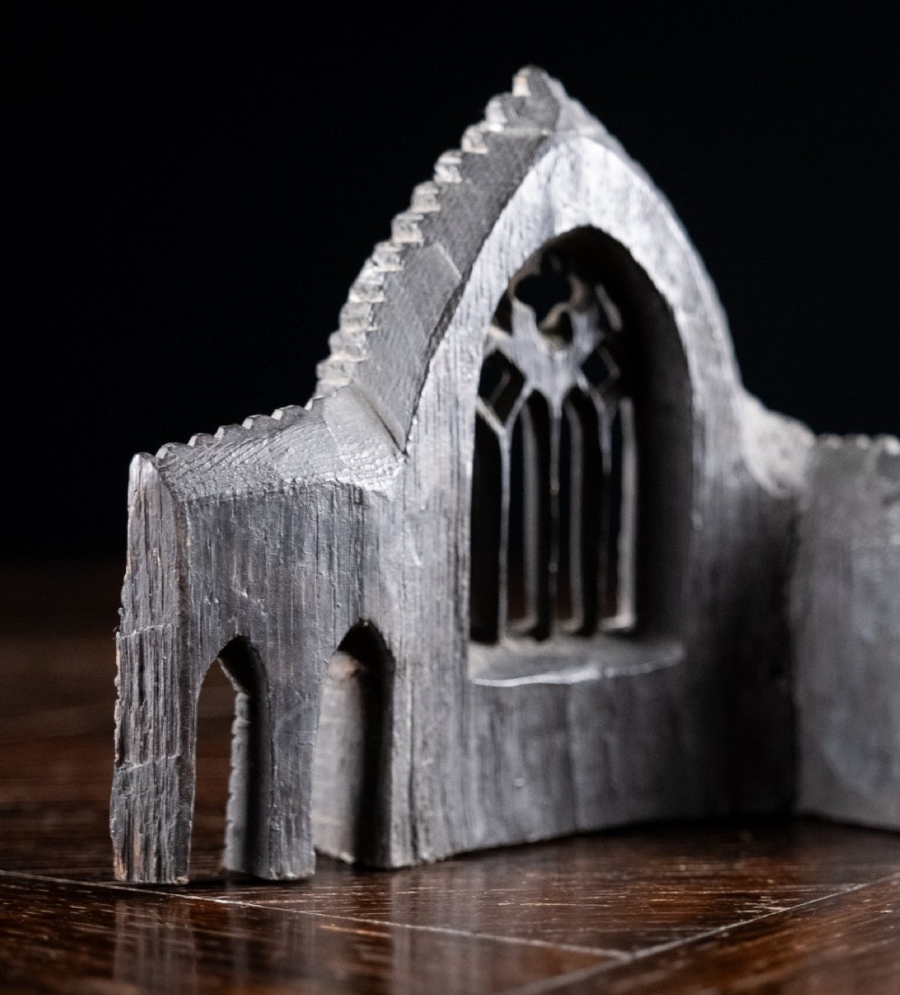 A dark hand-carved bog oak miniature representing a Gothic abbey architectural ruin with a tracery window and relief masonry wall. View IX