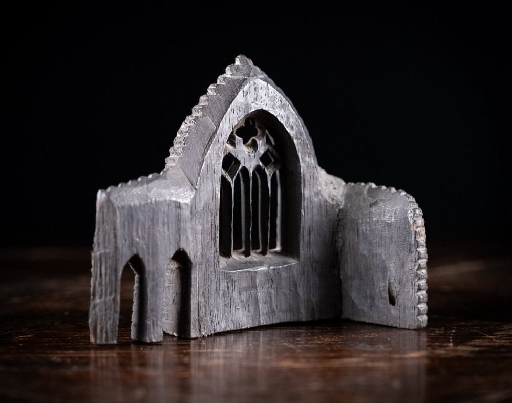 A dark hand-carved bog oak miniature representing a Gothic abbey architectural ruin with a tracery window and relief masonry wall. View X
