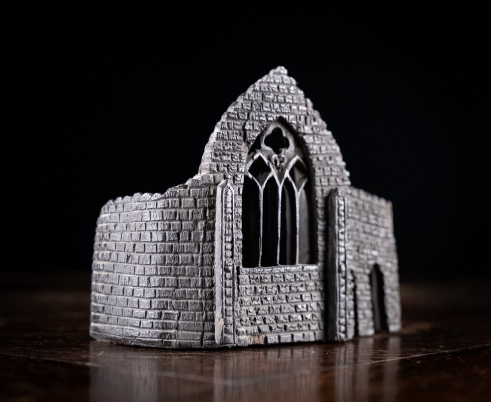 A dark hand-carved bog oak miniature representing a Gothic abbey architectural ruin with a tracery window and relief masonry wall. View XI