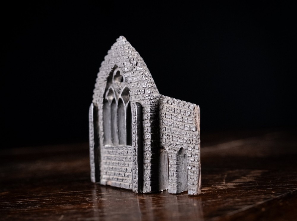 A dark hand-carved bog oak miniature representing a Gothic abbey architectural ruin with a tracery window and relief masonry wall. View XII