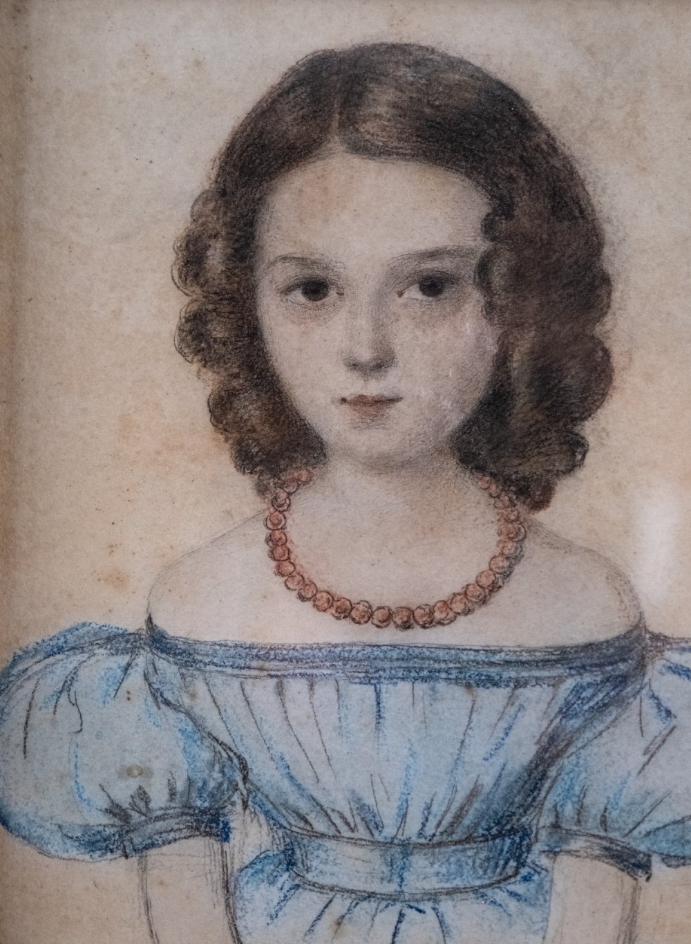 An early 19th-century watercolour portrait miniature depicting a young girl with dark curls in a blue dress, displayed in a dark wood frame. View II