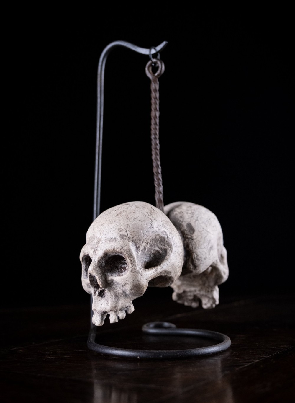 Two miniature carved skulls suspended by a metal chain from a black iron display stand.