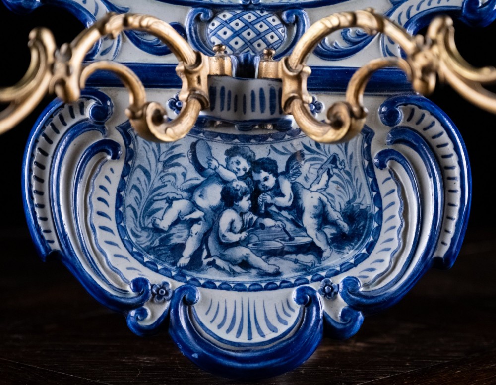 A late nineteenth-century blue and white ceramic wall sconce featuring Rococo scrollwork framing painted architectural and cherub motifs, fitted with two gilt bronze candle arms. View IV