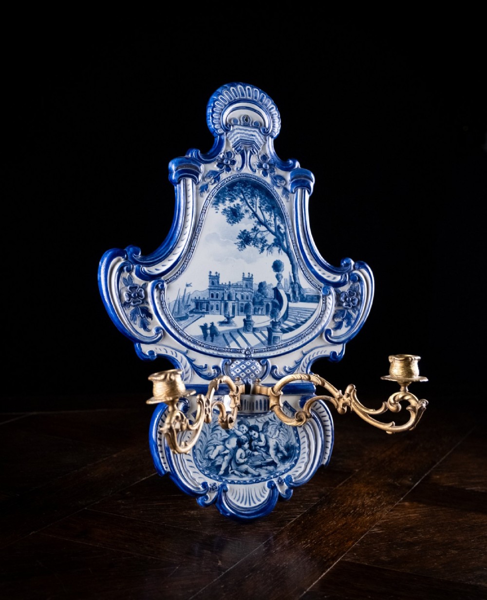A late nineteenth-century blue and white ceramic wall sconce featuring Rococo scrollwork framing painted architectural and cherub motifs, fitted with two gilt bronze candle arms. View XI