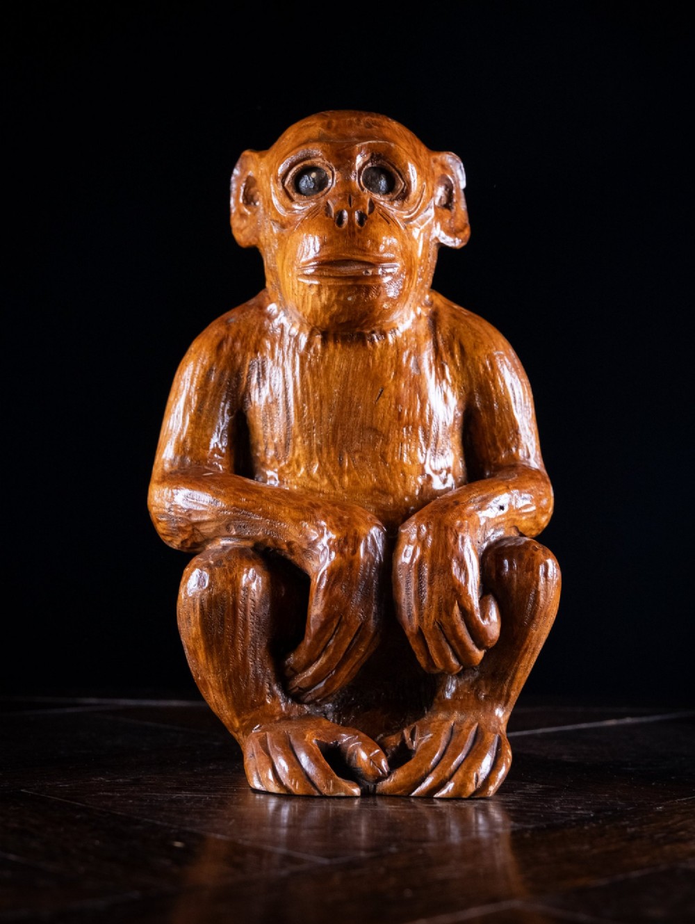 A hand-carved warm brown wooden sculpture depicting a seated monkey with chiselled fur texture.
