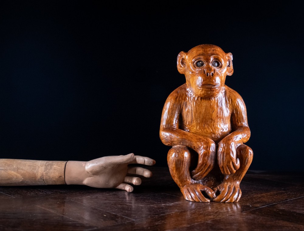 A hand-carved warm brown wooden sculpture depicting a seated monkey with chiselled fur texture. View II