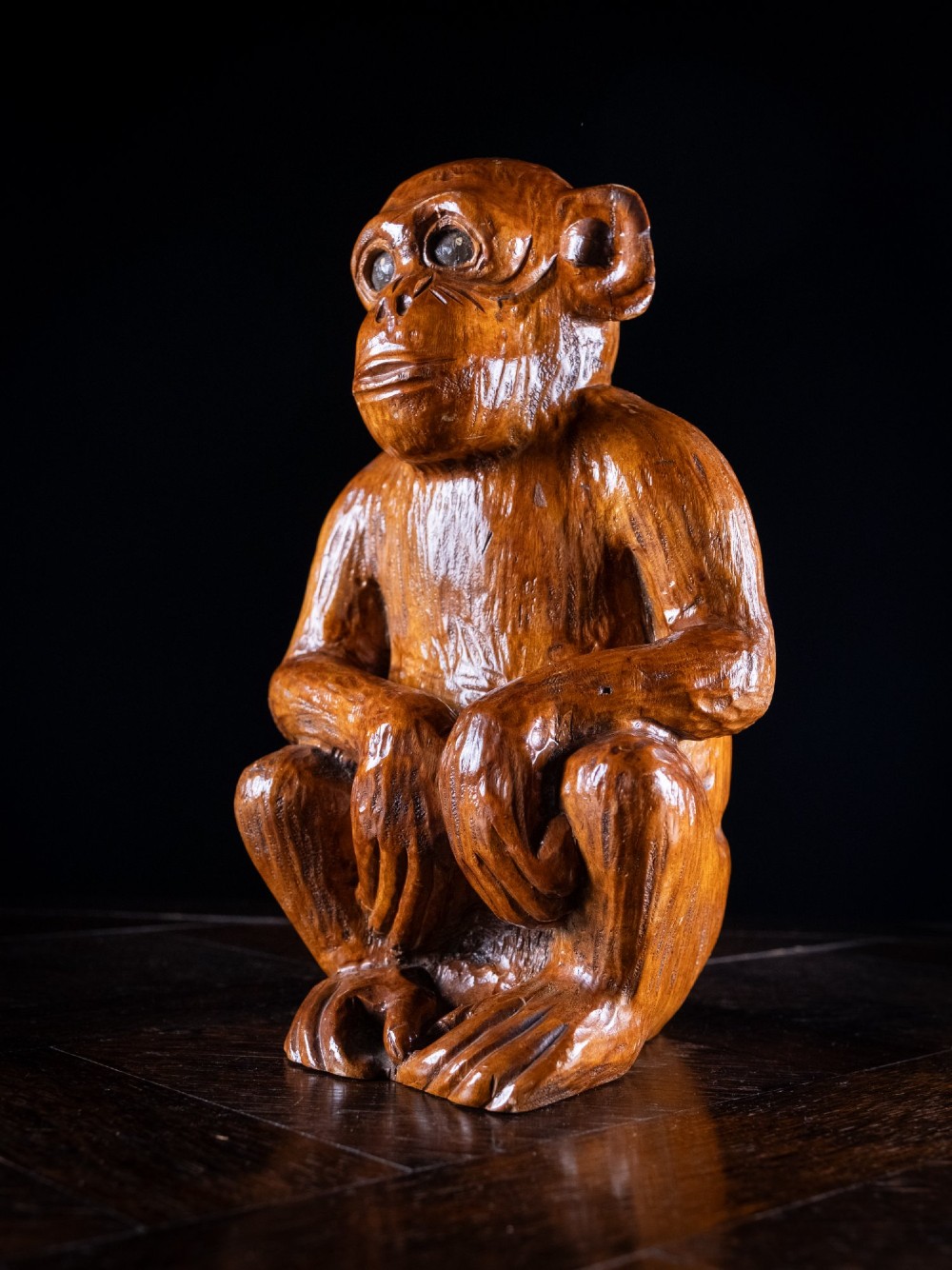 A hand-carved warm brown wooden sculpture depicting a seated monkey with chiselled fur texture. View VIII