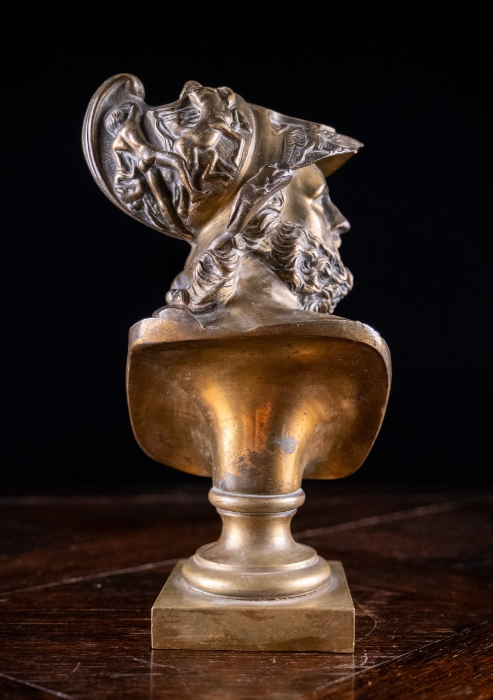 A profile view of a gilt bronze classical bust depicting a bearded warrior in a relief helmet set on a square pedestal base. View VIII