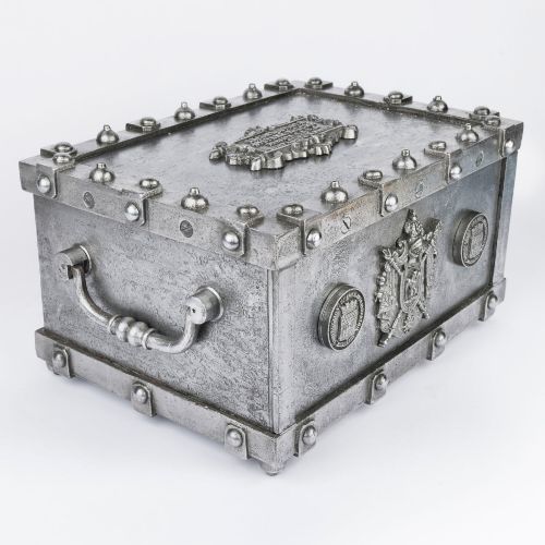 fig 2. A heavy rectangular metal strongbox featuring riveted steel straps, raised studs, an embossed coat of arms, and maker plaques.