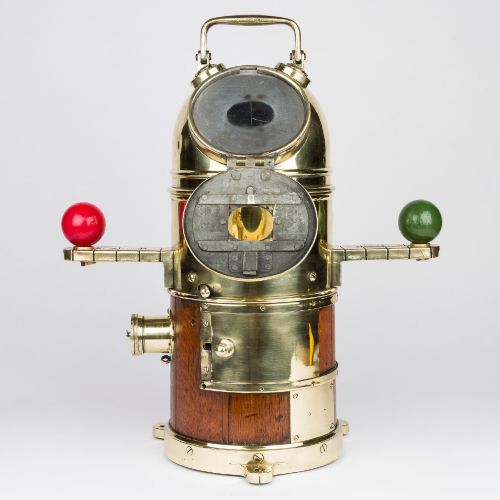 fig 1. A polished brass and mahogany submarine binnacle featuring a hinged hood with carrying handle, a glass viewing lens, and extended side arms holding red and green painted iron spheres.