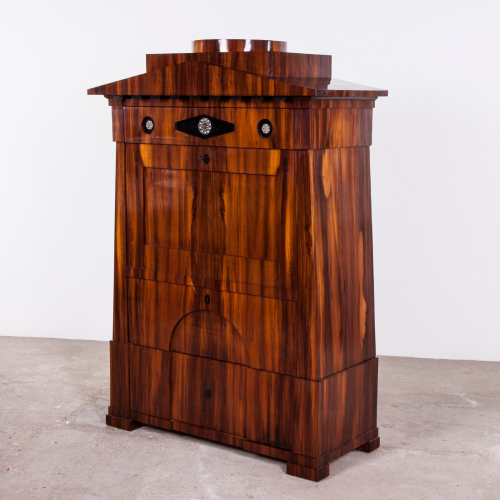 A tall Biedermeier secretaire a abattant featuring rich bookmatched brown wood veneers, an architectural pediment top, a fall-front desk section, and lower drawers with ebonised detail.