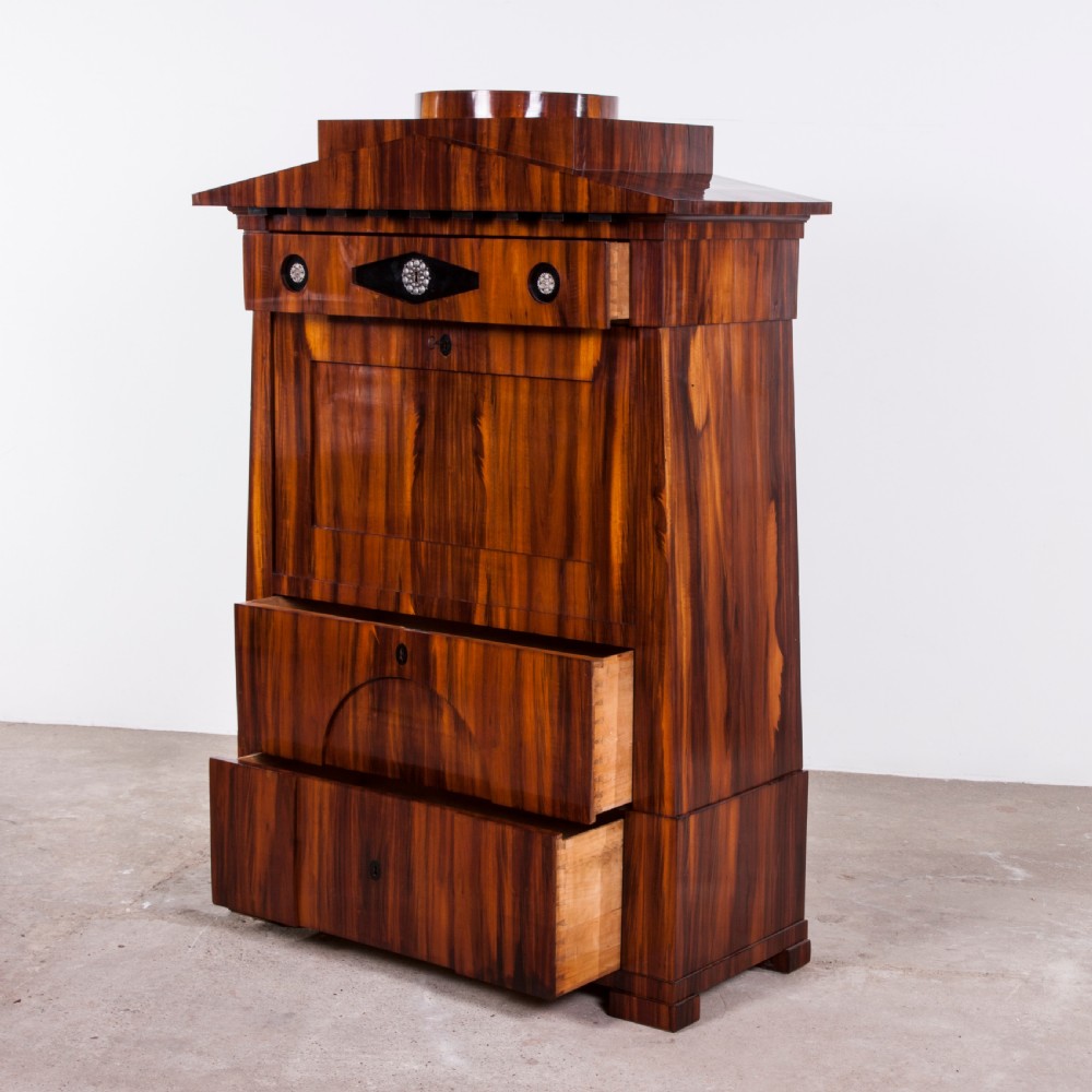 A tall Biedermeier secretaire a abattant featuring rich bookmatched brown wood veneers, an architectural pediment top, a fall-front desk section, and lower drawers with ebonised detail. View IV