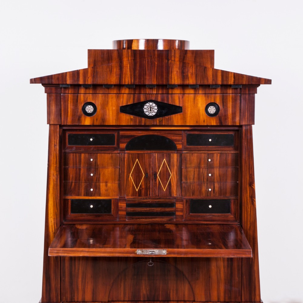 A tall Biedermeier secretaire a abattant featuring rich bookmatched brown wood veneers, an architectural pediment top, a fall-front desk section, and lower drawers with ebonised detail. View VI