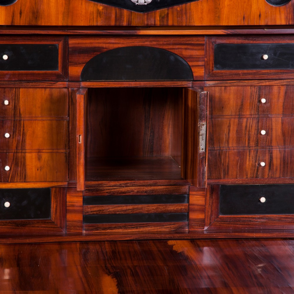 A tall Biedermeier secretaire a abattant featuring rich bookmatched brown wood veneers, an architectural pediment top, a fall-front desk section, and lower drawers with ebonised detail. View VIII