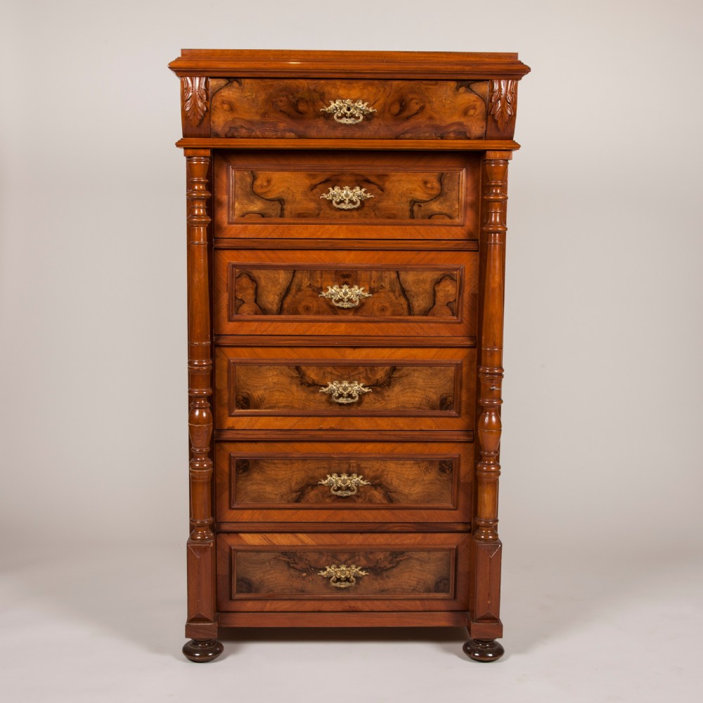 A tall 19th-century burr walnut chest of six drawers featuring ornate gilded brass handles, flanking turned pilasters, and bun feet.