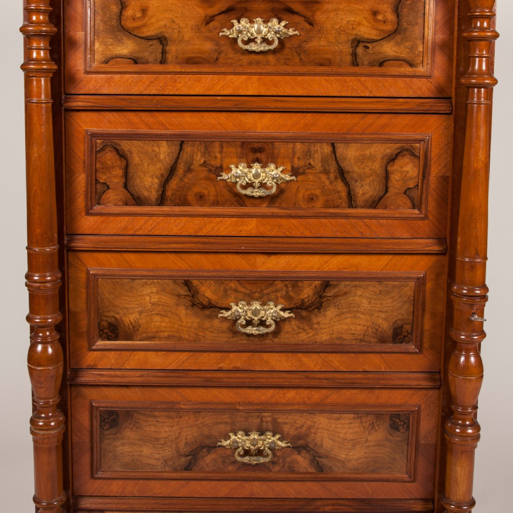 A tall 19th-century burr walnut chest of six drawers featuring ornate gilded brass handles, flanking turned pilasters, and bun feet. View IV