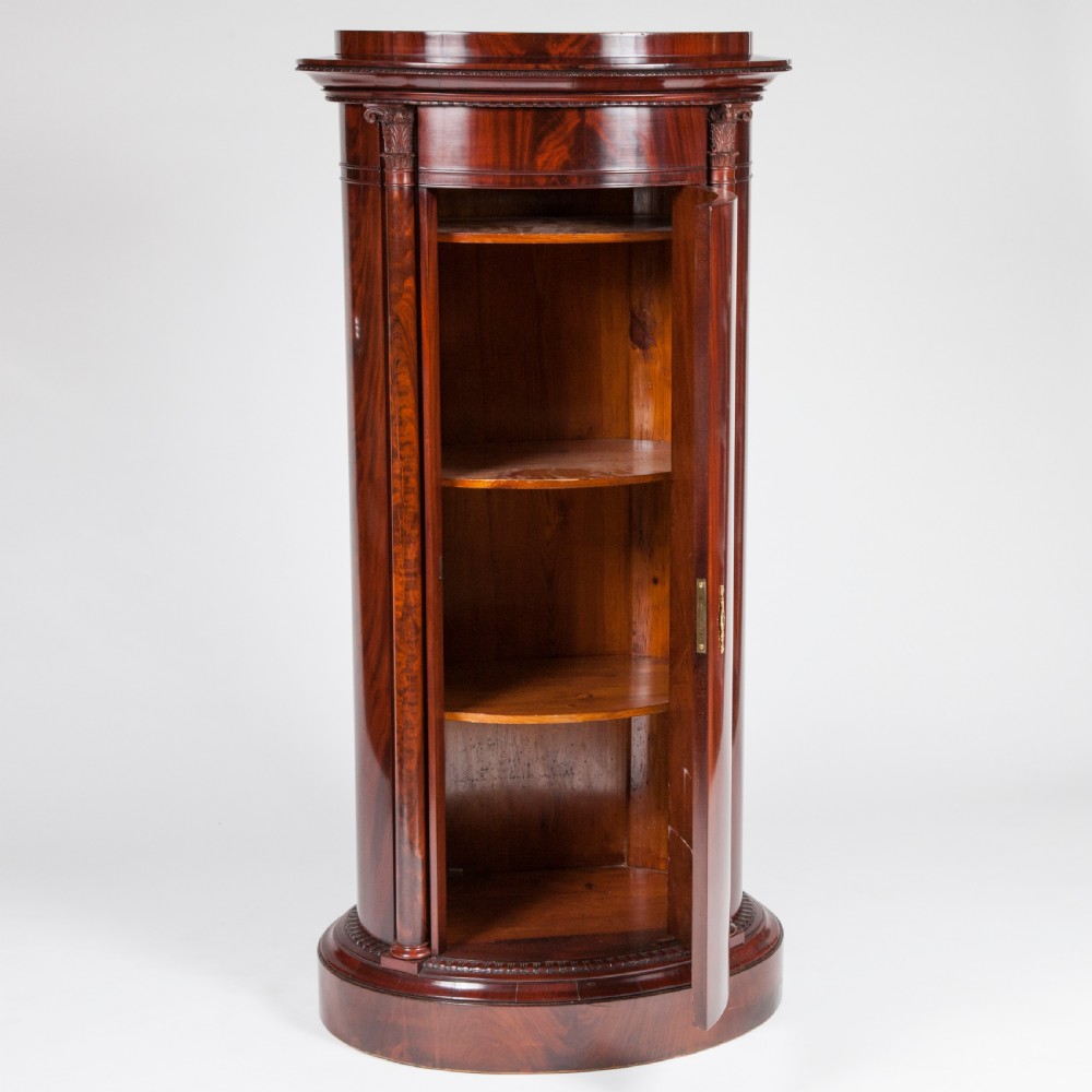 An antique Danish oval pedestal cabinet in polished flame mahogany featuring a single curved door, carved pilaster columns, and a brass keyhole escutcheon. View II