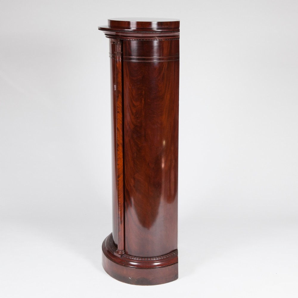 An antique Danish oval pedestal cabinet in polished flame mahogany featuring a single curved door, carved pilaster columns, and a brass keyhole escutcheon. View III