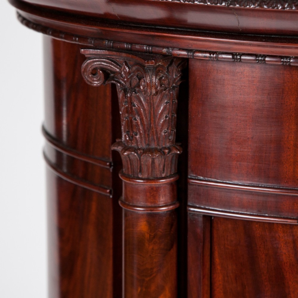 An antique Danish oval pedestal cabinet in polished flame mahogany featuring a single curved door, carved pilaster columns, and a brass keyhole escutcheon. View V