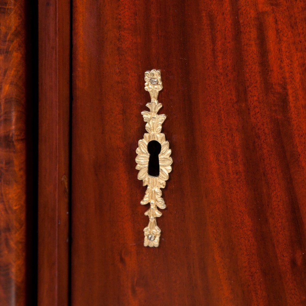 An antique Danish oval pedestal cabinet in polished flame mahogany featuring a single curved door, carved pilaster columns, and a brass keyhole escutcheon. View VII