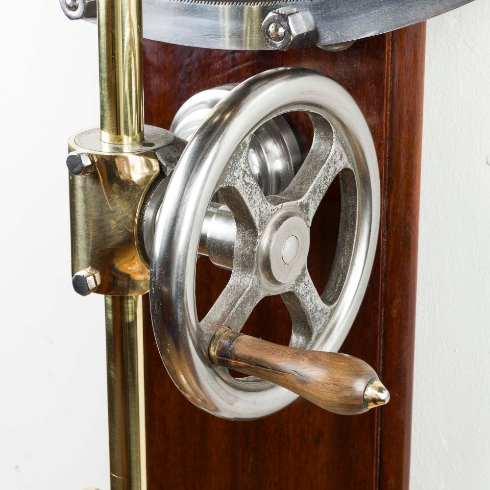 A wall-mounted antique Goodbrand & Co brass and steel yarn testing instrument mounted on a rectangular mahogany board with a circular dial scale. View III