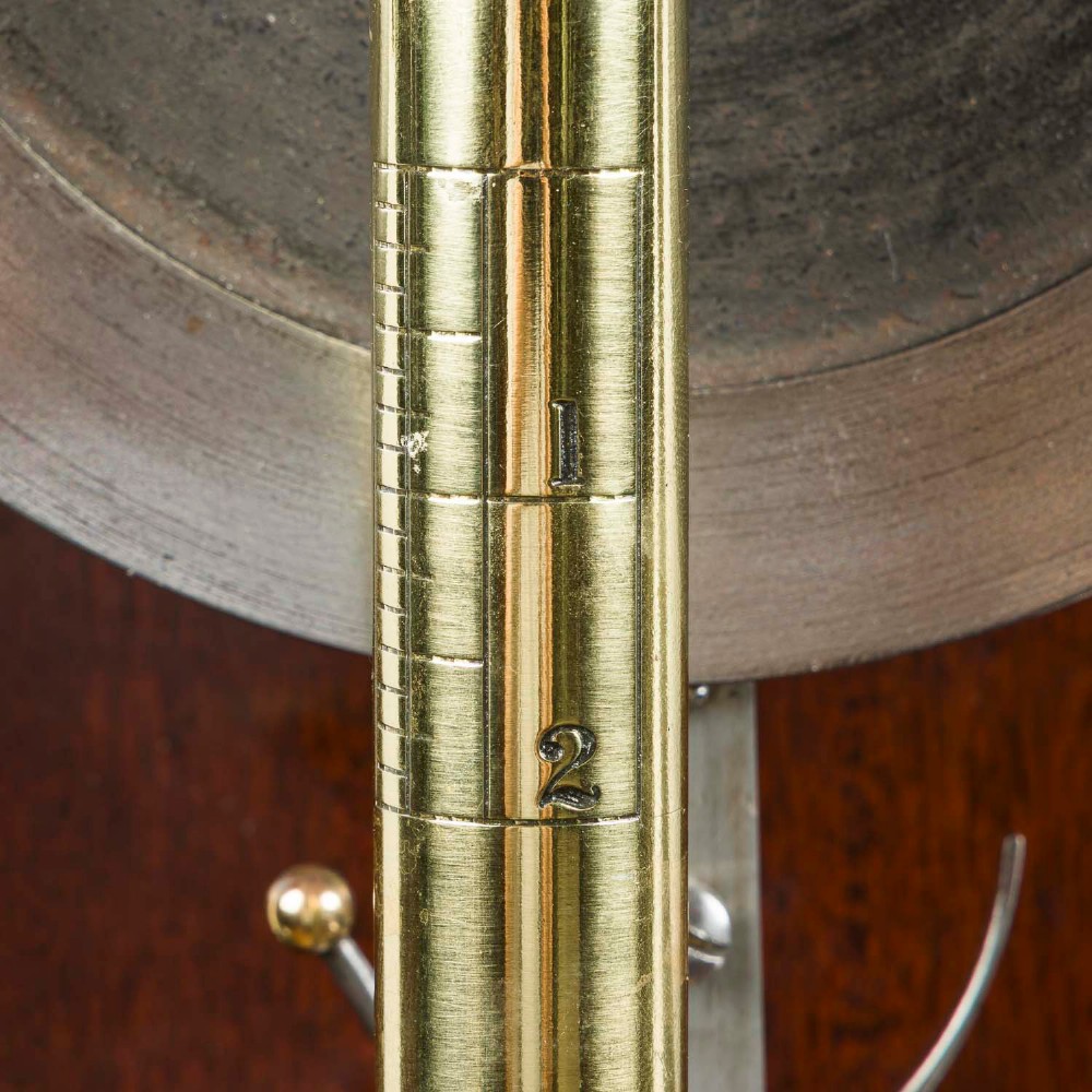 A wall-mounted antique Goodbrand & Co brass and steel yarn testing instrument mounted on a rectangular mahogany board with a circular dial scale. View V