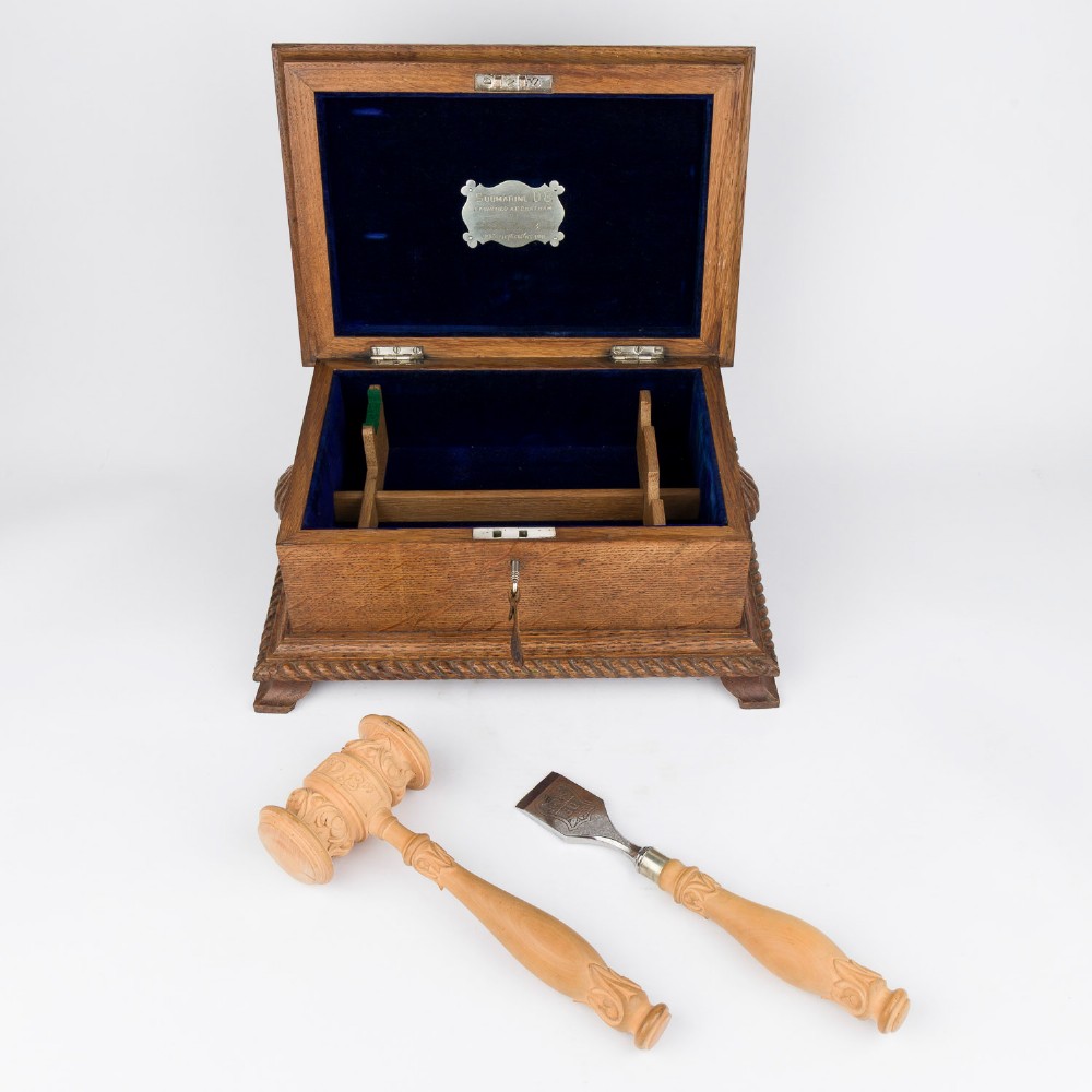 An open Edwardian carved oak presentation casket lined in navy blue velvet, containing a carved wooden ceremonial mallet and chisel set with an engraved silver plaque. View III