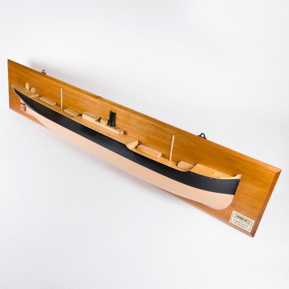 A half hull ship model of the S.S. Othello painted black and cream mounted horizontally on a rectangular mahogany backboard with a metal builder plaque. View II