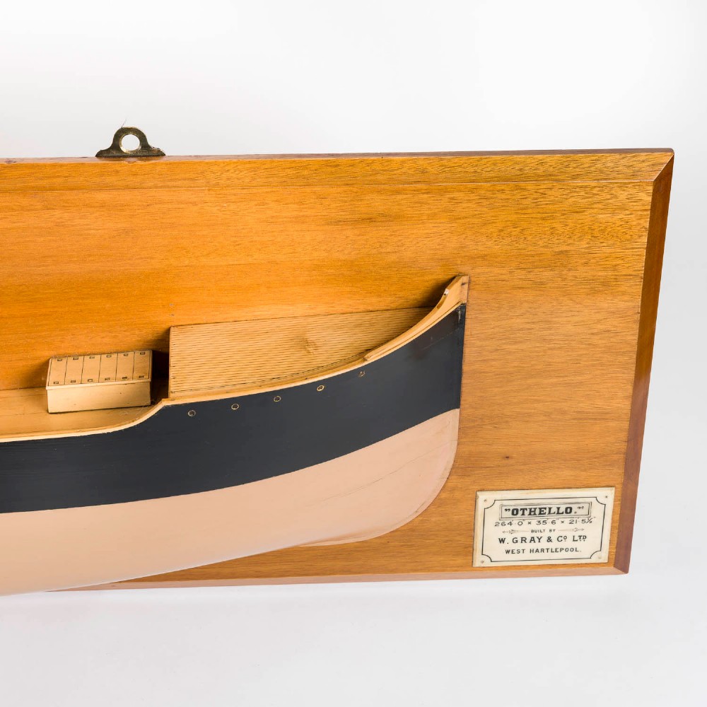 A half hull ship model of the S.S. Othello painted black and cream mounted horizontally on a rectangular mahogany backboard with a metal builder plaque. View III