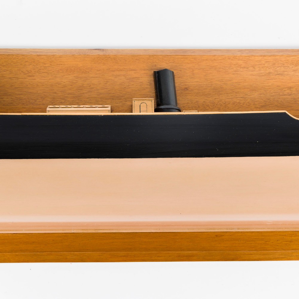 A half hull ship model of the S.S. Othello painted black and cream mounted horizontally on a rectangular mahogany backboard with a metal builder plaque. View IV