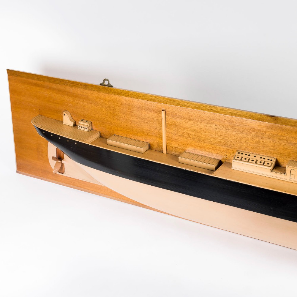 A half hull ship model of the S.S. Othello painted black and cream mounted horizontally on a rectangular mahogany backboard with a metal builder plaque. View V