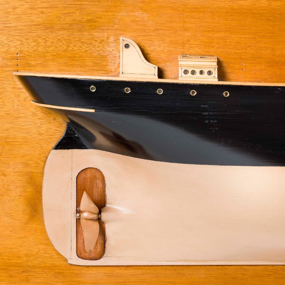 A half hull ship model of the S.S. Othello painted black and cream mounted horizontally on a rectangular mahogany backboard with a metal builder plaque. View VI