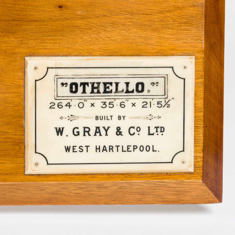 A half hull ship model of the S.S. Othello painted black and cream mounted horizontally on a rectangular mahogany backboard with a metal builder plaque. View VIII
