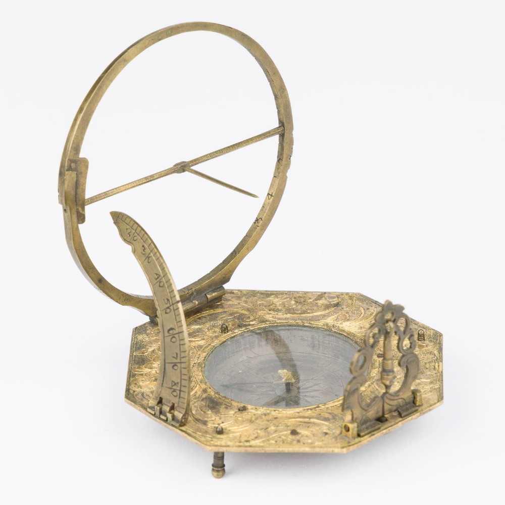 An 18th-century engraved brass octagonal pocket sundial with an inset glass-covered compass, an adjustable latitude arc, and a hinged hour ring.