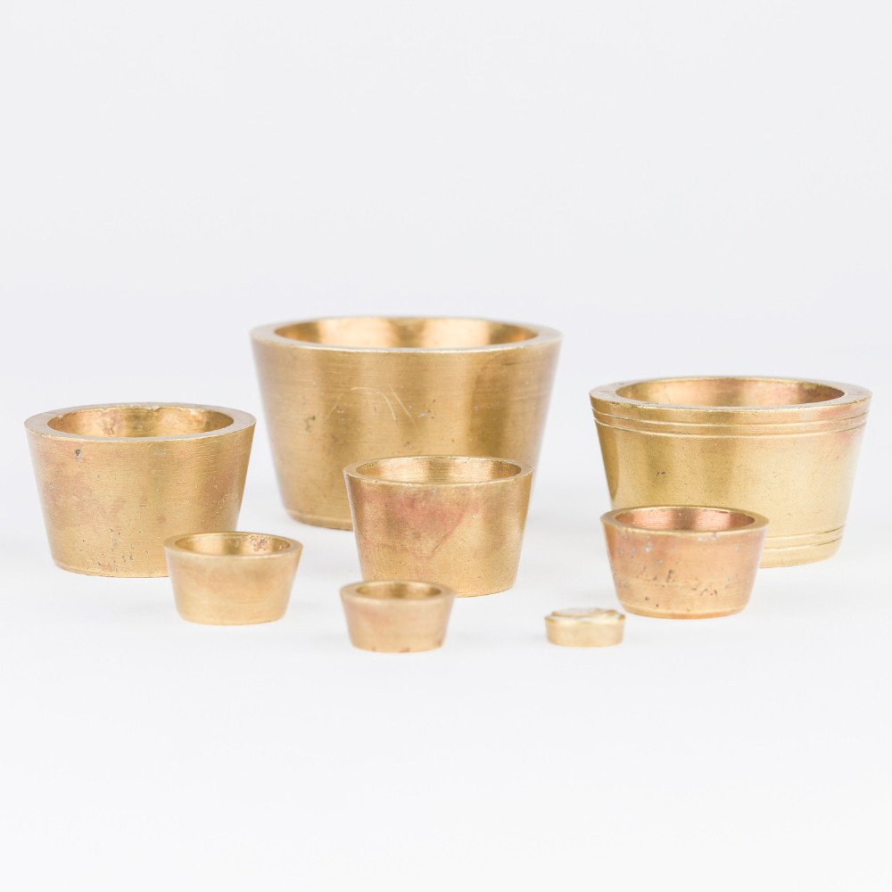 A set of eight graduated cylindrical brass nesting cup weights arranged in two loose rows on a plain white surface.