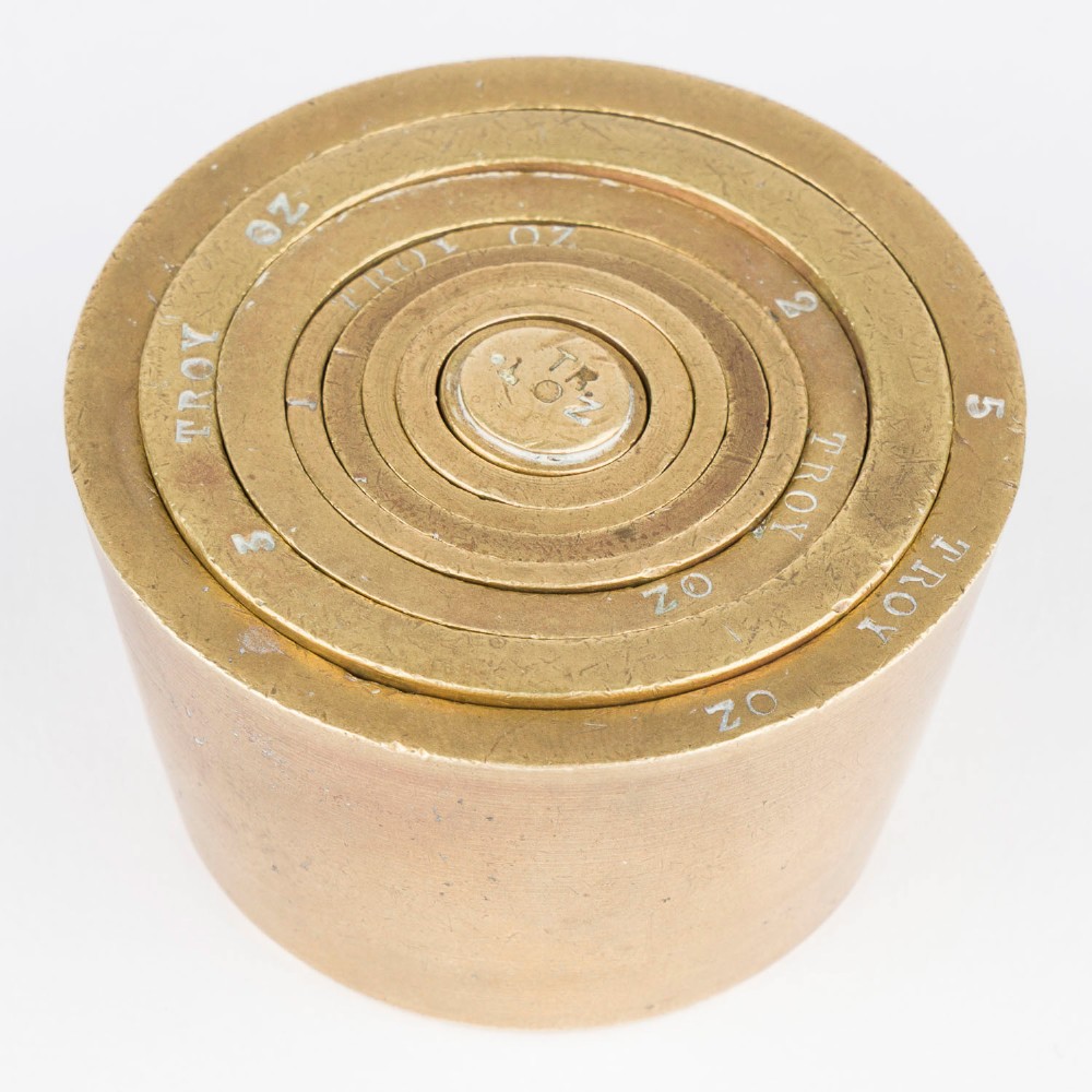 A set of eight graduated cylindrical brass nesting cup weights arranged in two loose rows on a plain white surface. View II