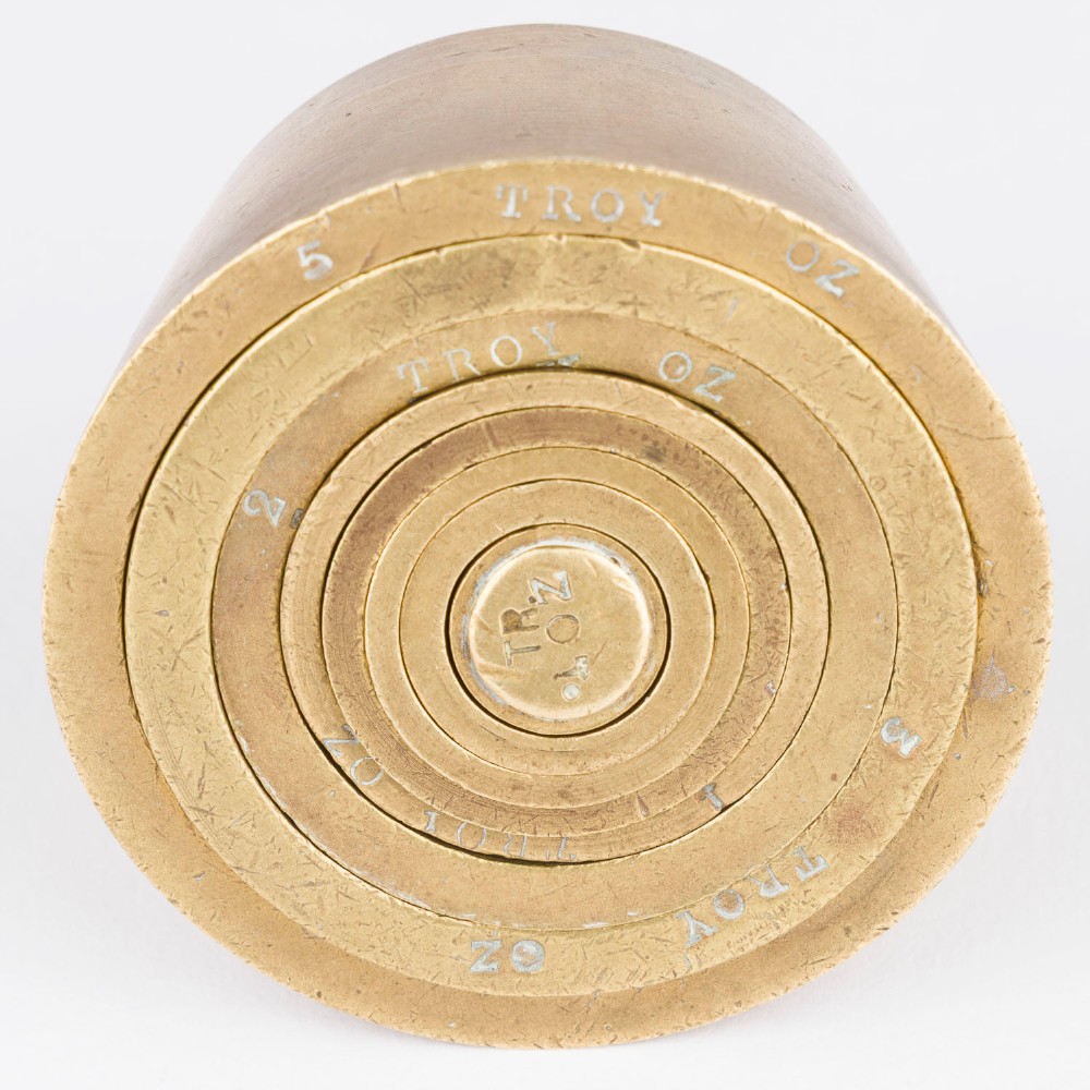 A set of eight graduated cylindrical brass nesting cup weights arranged in two loose rows on a plain white surface. View III